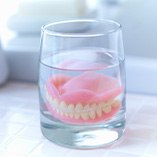 Full set of dentures in a glass of clear fluid on a tiled countertop