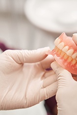 White-gloved hands holding complete set of dentures