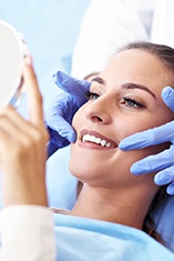 Woman examining her smile with an implant dentist in Park Slope