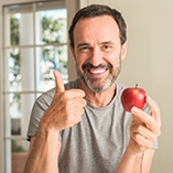 Man in grey t-shirt smiling with apple and thumb up