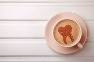 Pink cup of coffee with a tooth pattern in the foam on a white panel surface