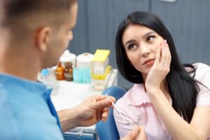 Woman with black hair in dentist's chair holding her jaw in pain